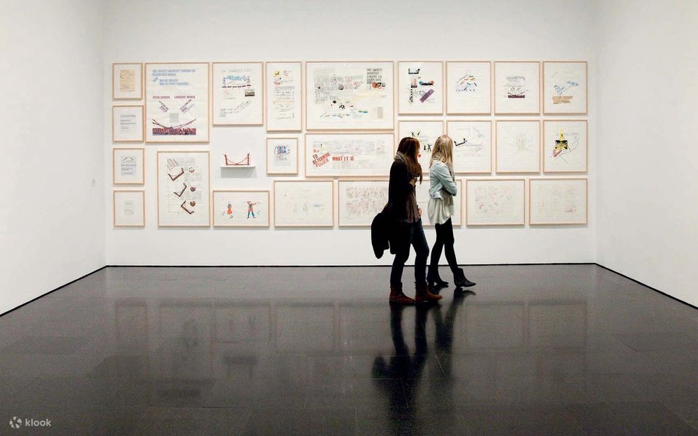 Visitors viewing framed contemporary artworks in a modern gallery with white walls.