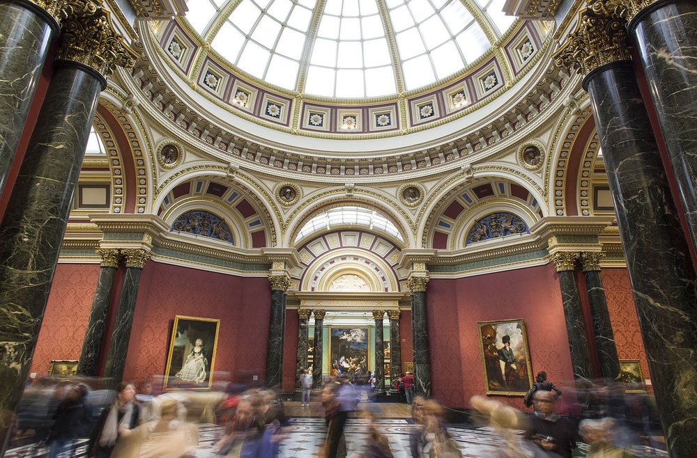 The red-walled interior of a museum with paintings on display