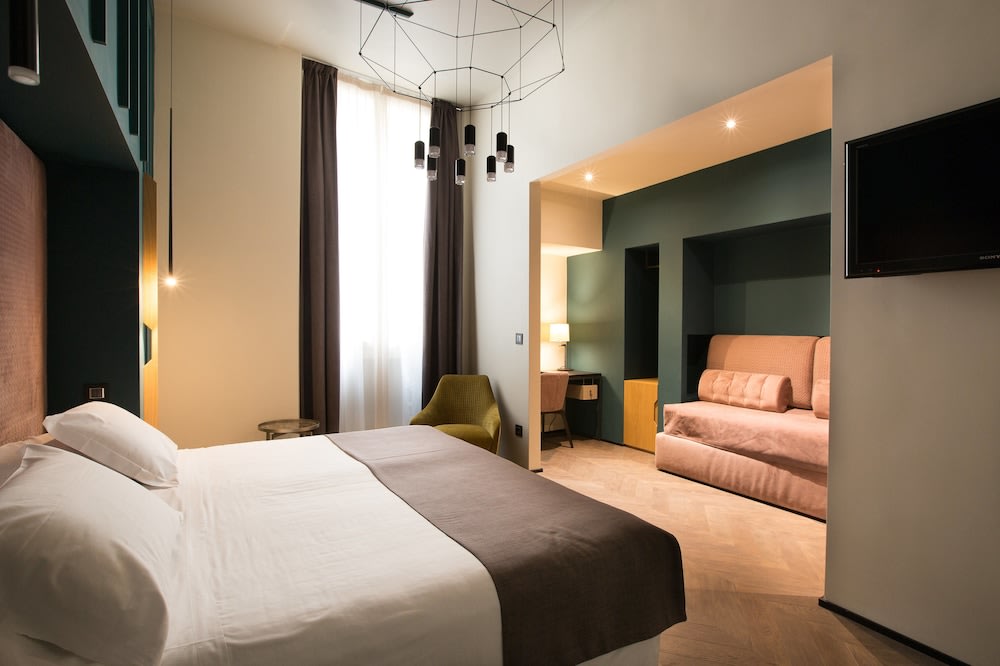 A spacious room, with a window beside the bed and a couch at the foot of it. Beside the couch is a study area