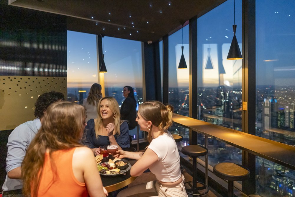 Group of friends having drinks at a Melbourne rooftop bar overlooking the city
