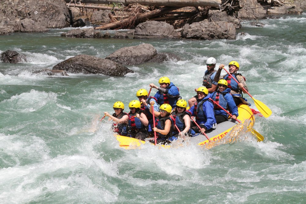 Group white water rafting through rapids while wearing helmets and life jackets | Photo Credit: Walter Rock on Pexels