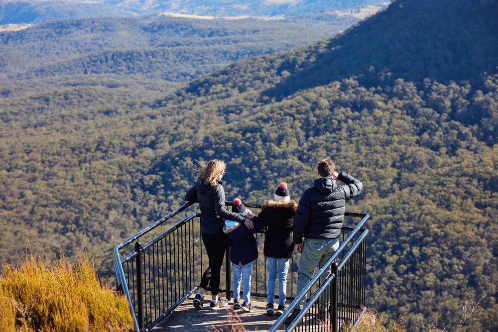 Visitors standing at a lookout overlooking forested valleys in the Blue Mountains