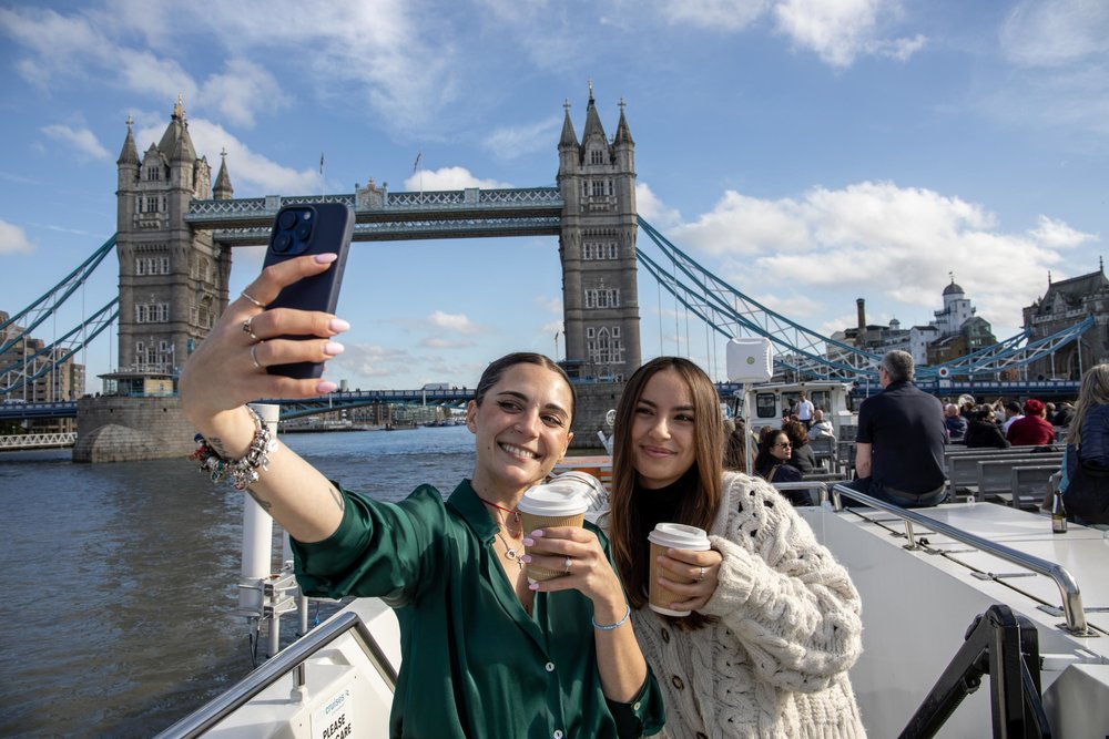 Two people taking a selfie on a Thames sightseeing cruise with Tower Bridge in the background