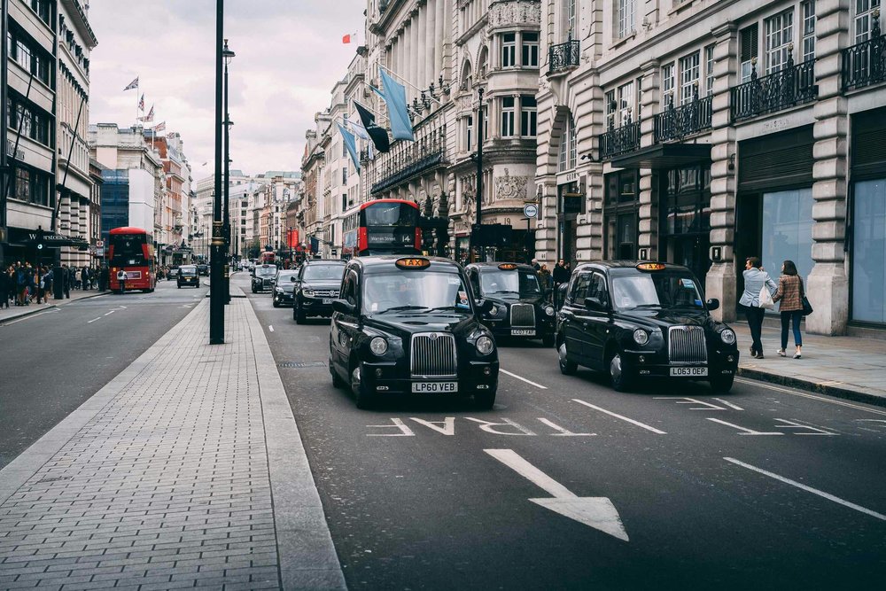 Black London taxis driving along a busy city street with red buses | Photo Credit: Ferdinand Stöhr on Unsplash