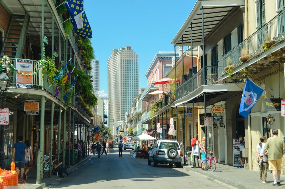 French Quarter street in New Orleans with balconies, flags, and people walking on a sunny day