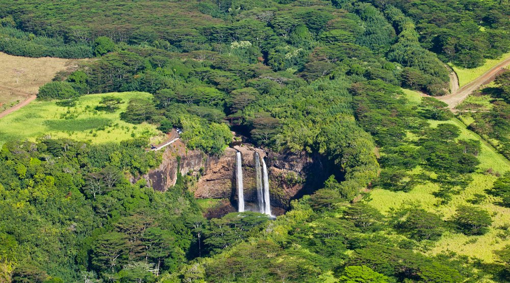 Aerial view of a waterfall surrounded by green valleys on the island of Kauai