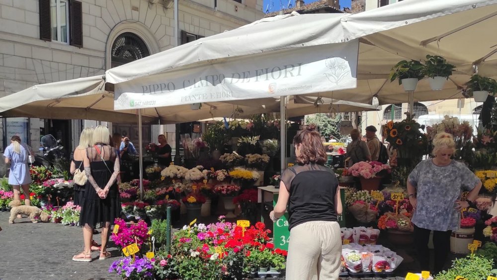 Flower stalls and locals at Campo de’ Fiori market in Rome on a sunny day