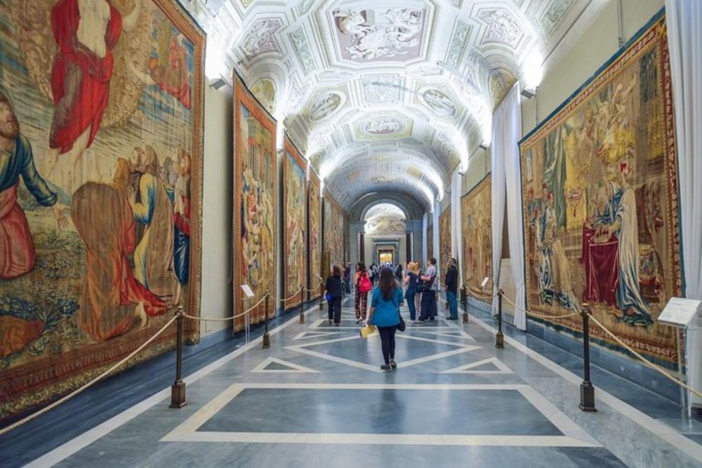 Visitors walking through a tapestry-filled gallery inside the Vatican Museums