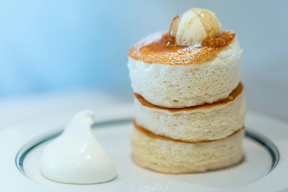 Japanese souffle pancakes stacked on top of each other, served with whipped cream.