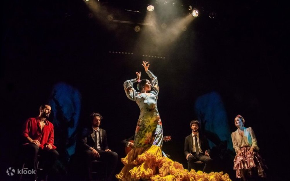 Flamenco dance class in Seville with a dancer performing on stage while musicians sit behind her.