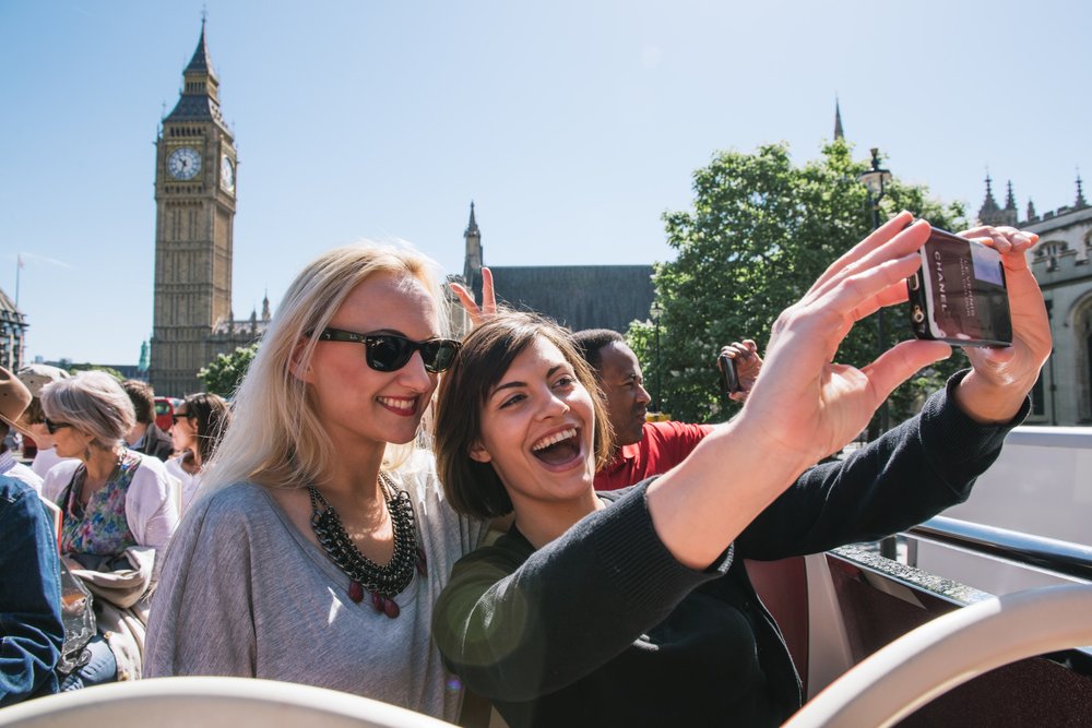 Travelers taking a selfie on a London sightseeing bus with Big Ben in the background