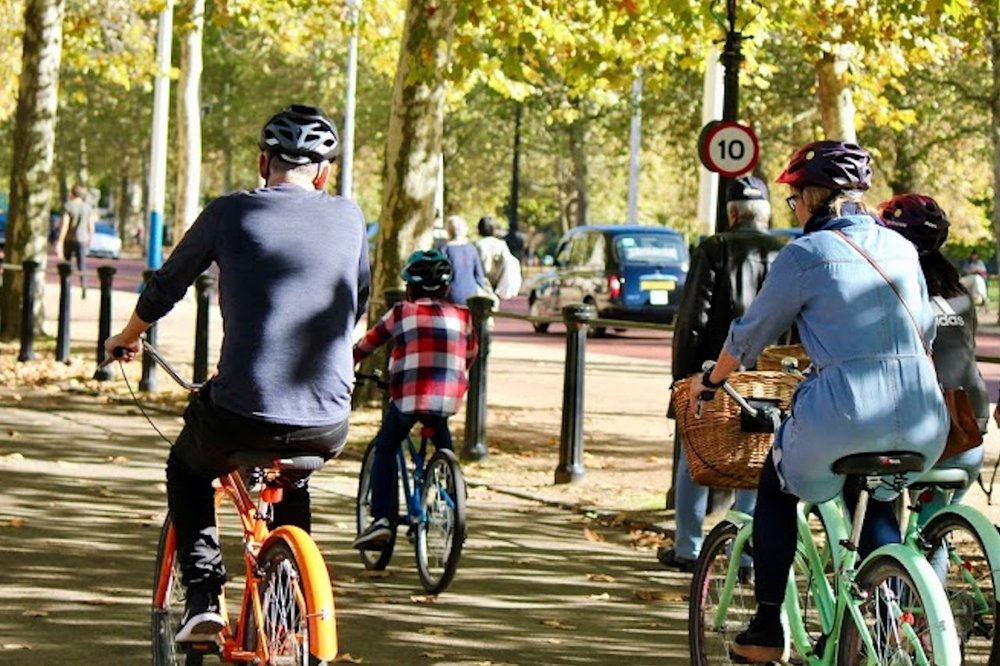 People riding bicycles along a tree-lined path in London during autumn