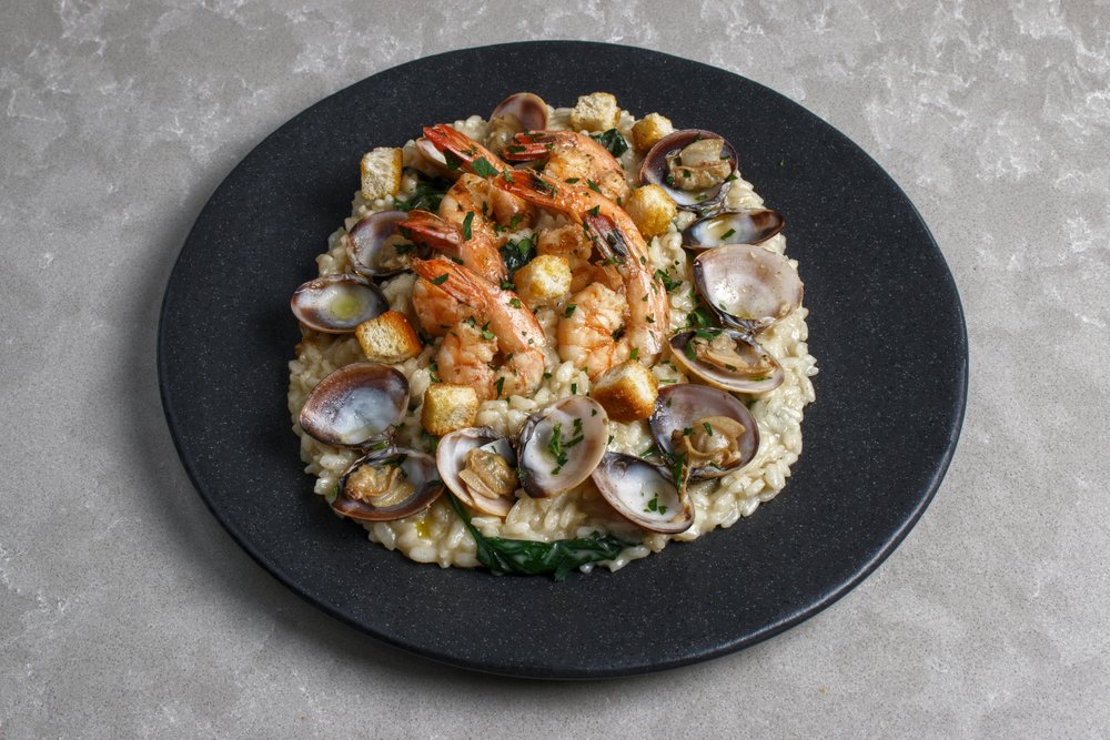 Creamy risotto Milanese with shrimp and clams served on a black plate