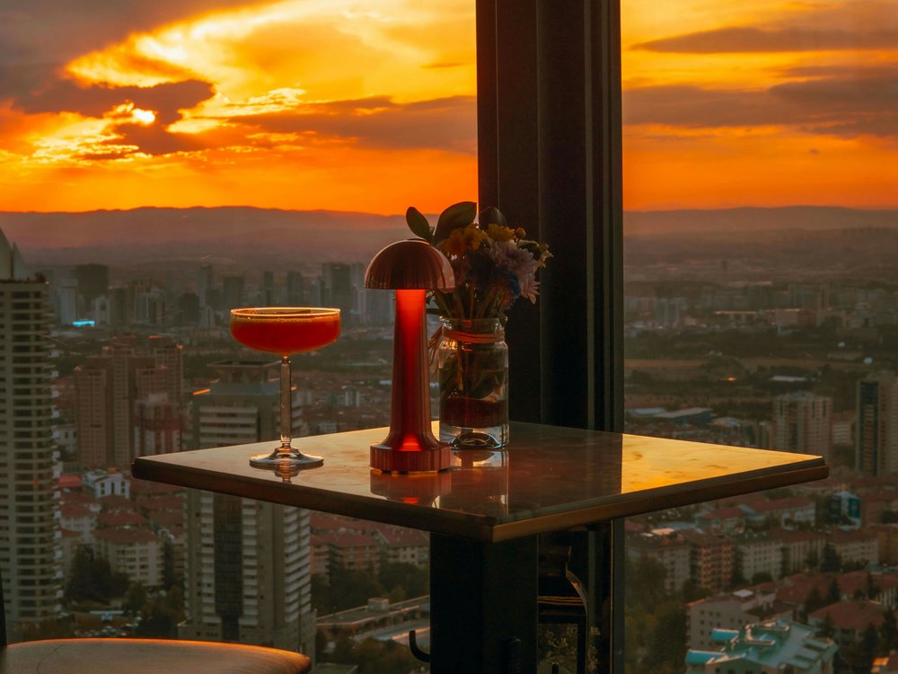 Cocktail on table overlooking Auckland skyline at sunset rooftop bar