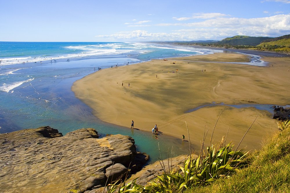 Wide stretch of black sand at Muriwai Beach on Auckland’s west coast | Photo Credit: Wikimedia Commons