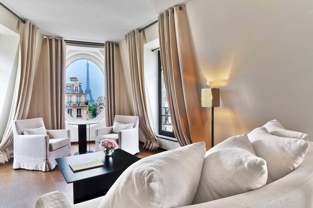 Stylish suite at Le Metropolitan Paris with seating area and a view of the Eiffel Tower through arched windows