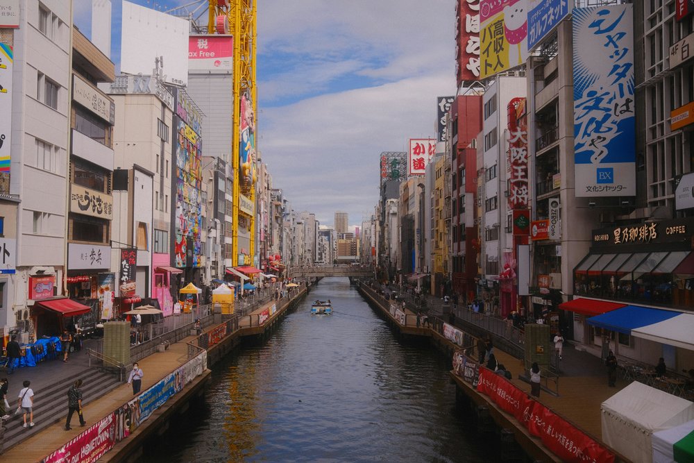 Busy Osaka street at daytime with neon signs and canal, a lively urban scene