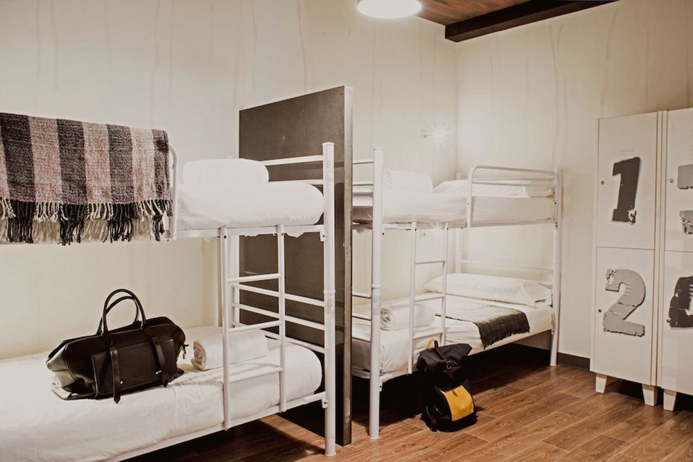 Youth hostel dorm room with bunk beds, lockers, and luggage space