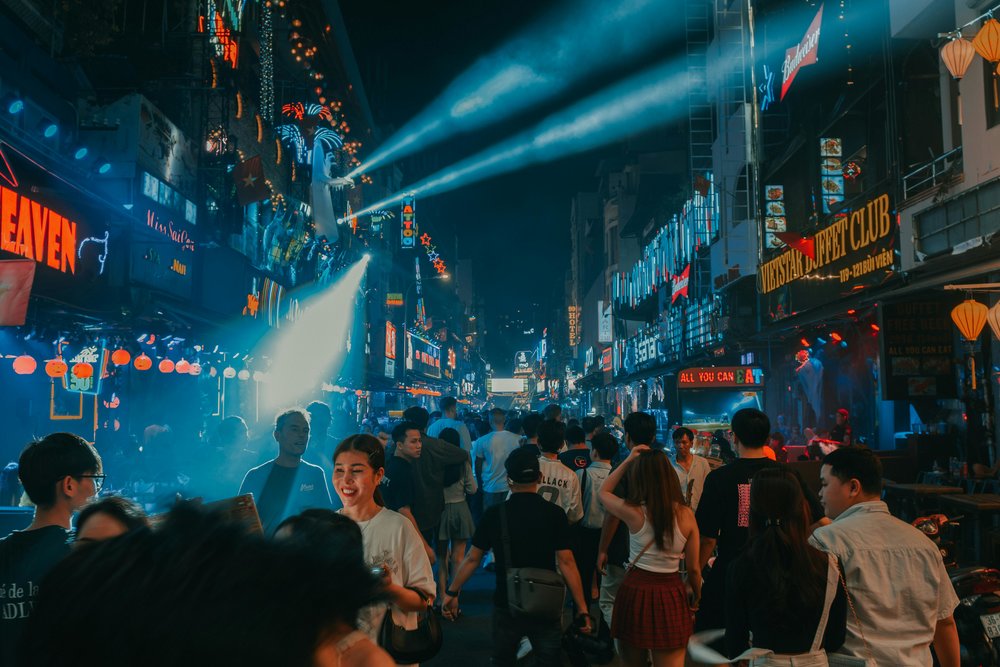 Busy nightlife street in Ho Chi Minh City packed with people, neon signs, and bars at night