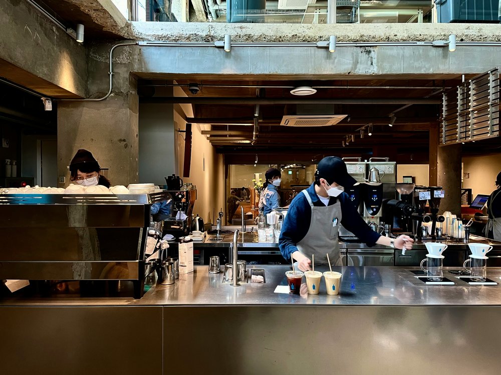 The interior of a cafe, with 3 people behind a counter preparing cups of coffee