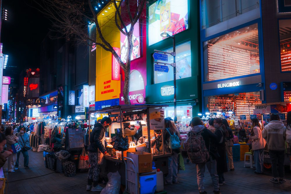 A crowded street full of people, vendor stalls, and illuminated storefronts