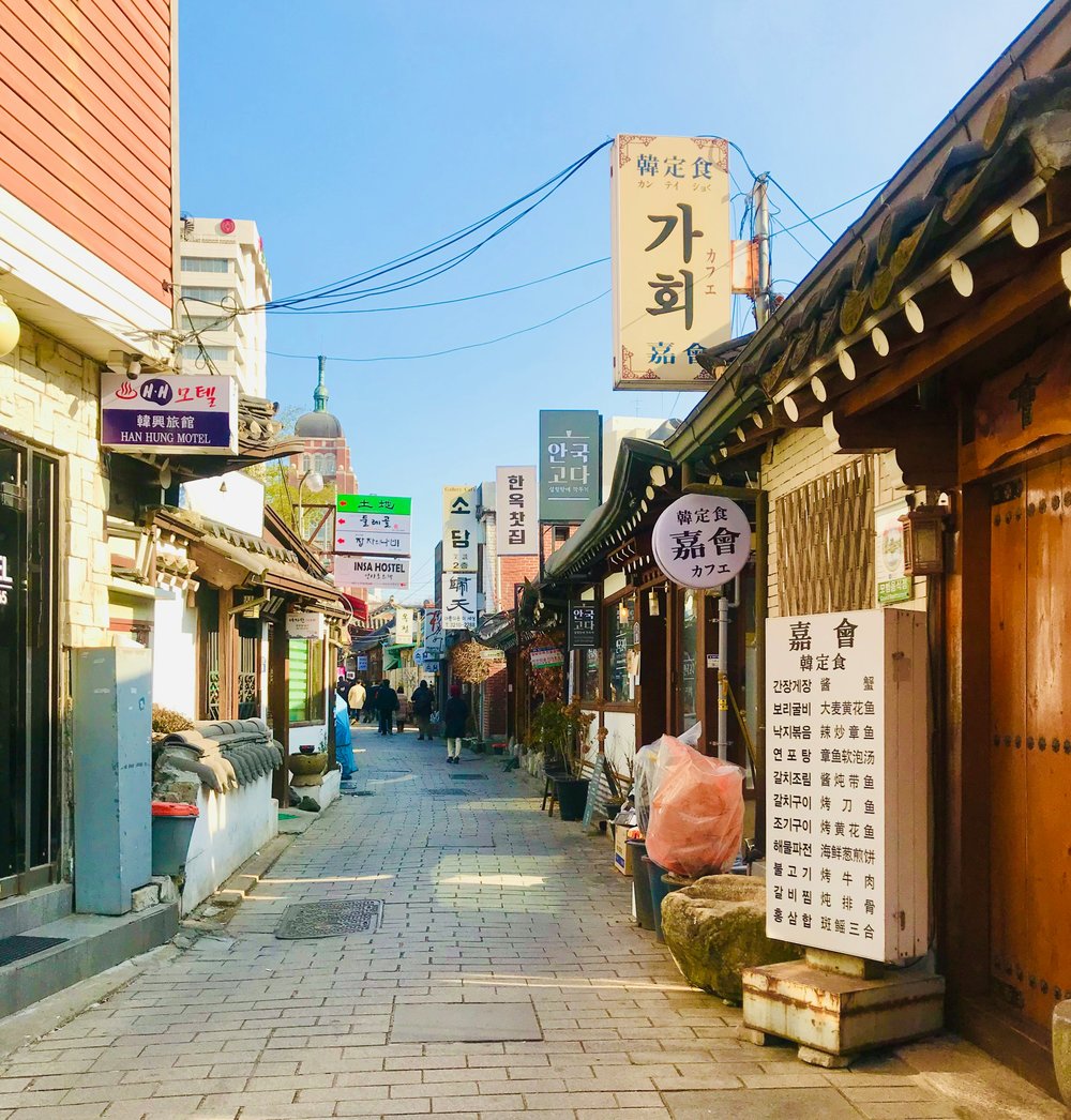 A narrow tiled pathway lined with stores and Korean-language signs