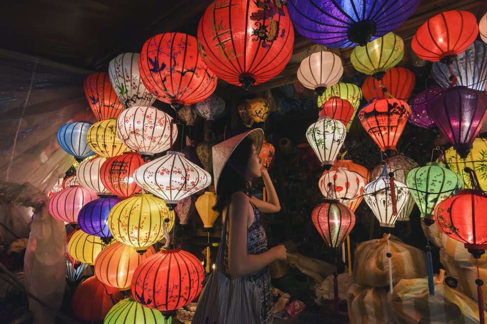 Woman wearing a conical hat admiring colourful lanterns inside a Hoi An shop
