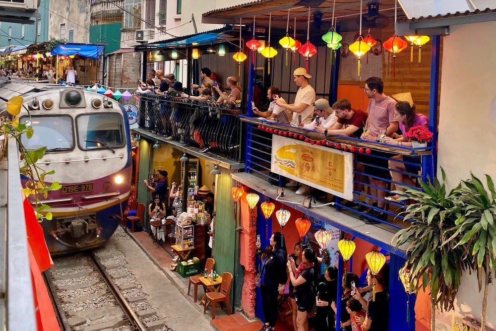 Train passing through Hanoi Train Street with tourists watching from nearby cafés