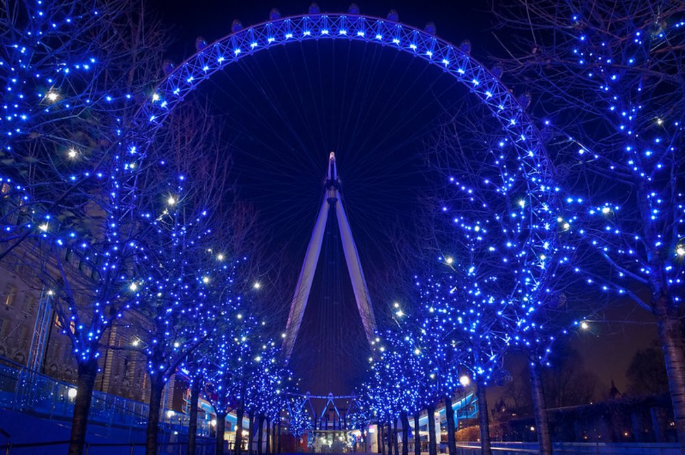 London Eye glowing blue in winter with holiday lights on South Bank