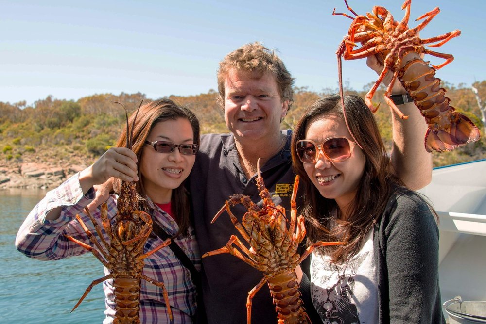 Travellers holding freshly caught Tasmanian lobsters on seafood tour
