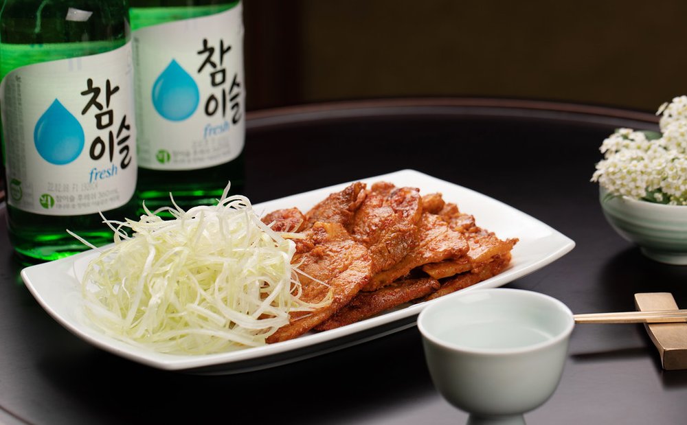 Bottles of soju next to a plate of grilled meat with vegetables | Photo Credit: Flickr