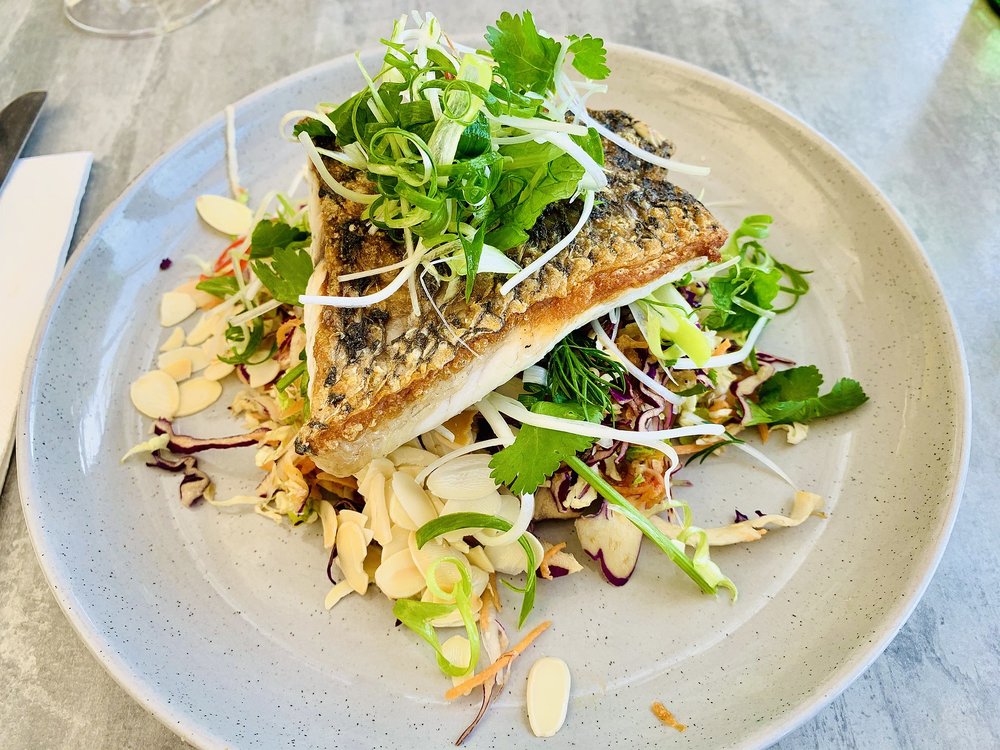 Grilled barramundi fillet topped with greens on a white plate