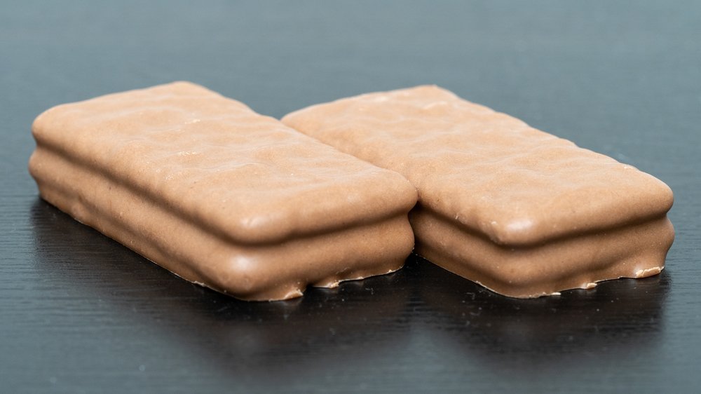 Two stacked Tim Tam chocolate biscuits on a dark surface