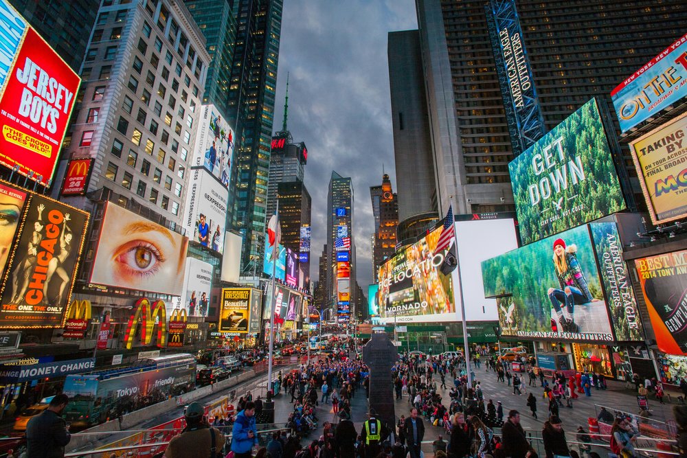 A very crowded city square surrounded by skyscrapers and large billboards