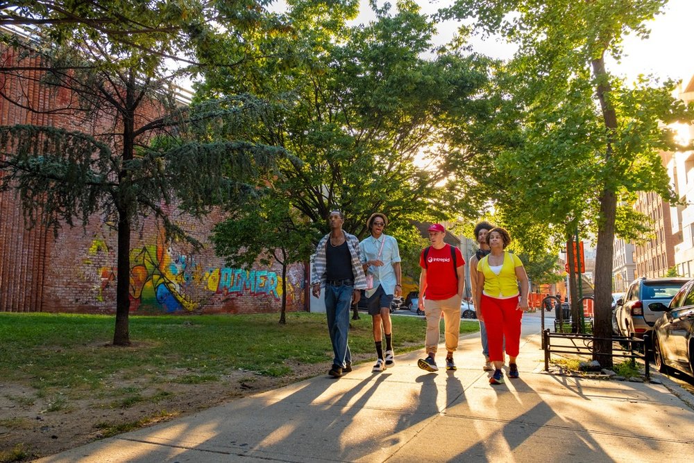 A small group of people walking on a sidewalk lined by trees