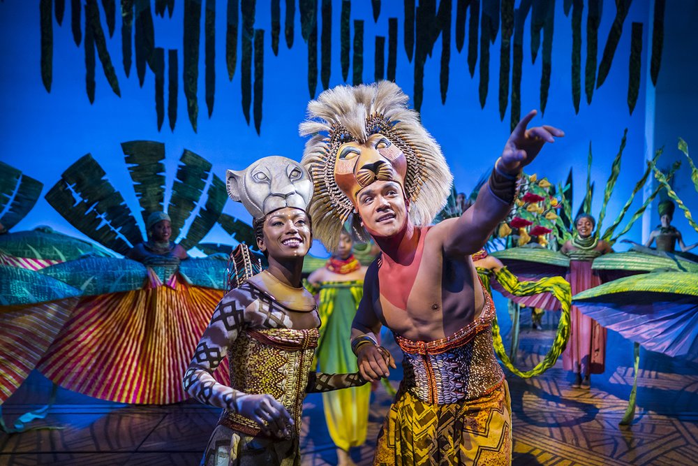 Actors performing The Lion King musical in London with colorful costumes and vibrant stage set