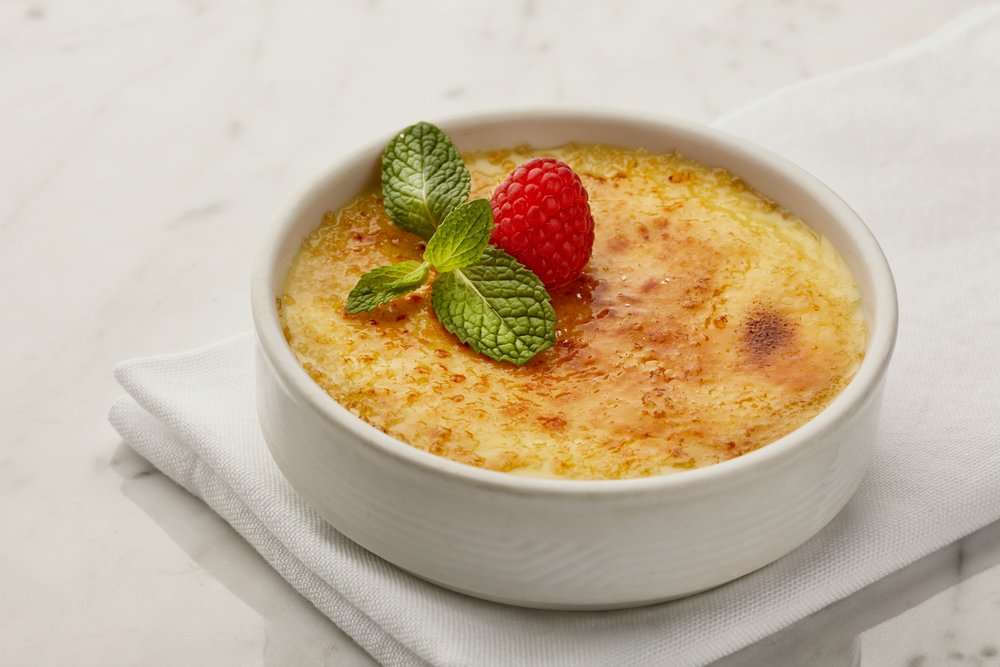 Crème brûlée in white ramekin with torched sugar crust and mint garnish
