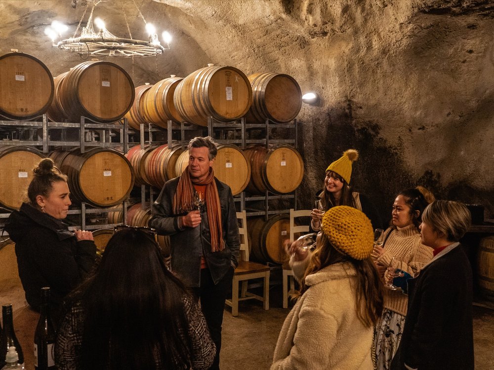 Group enjoying wine tasting in a rustic Queenstown cellar with oak barrels