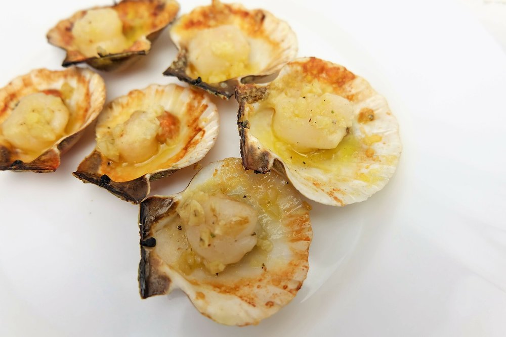 Baked scallops in shells topped with butter and herbs on a white plate