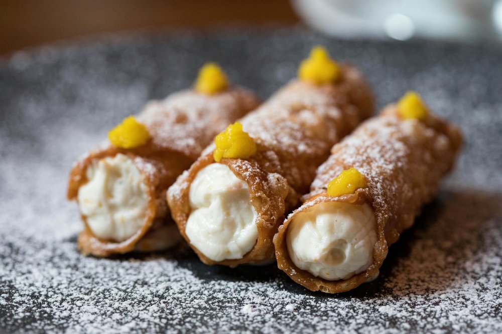 Three cannoli filled with cream and topped with citrus zest and sugar