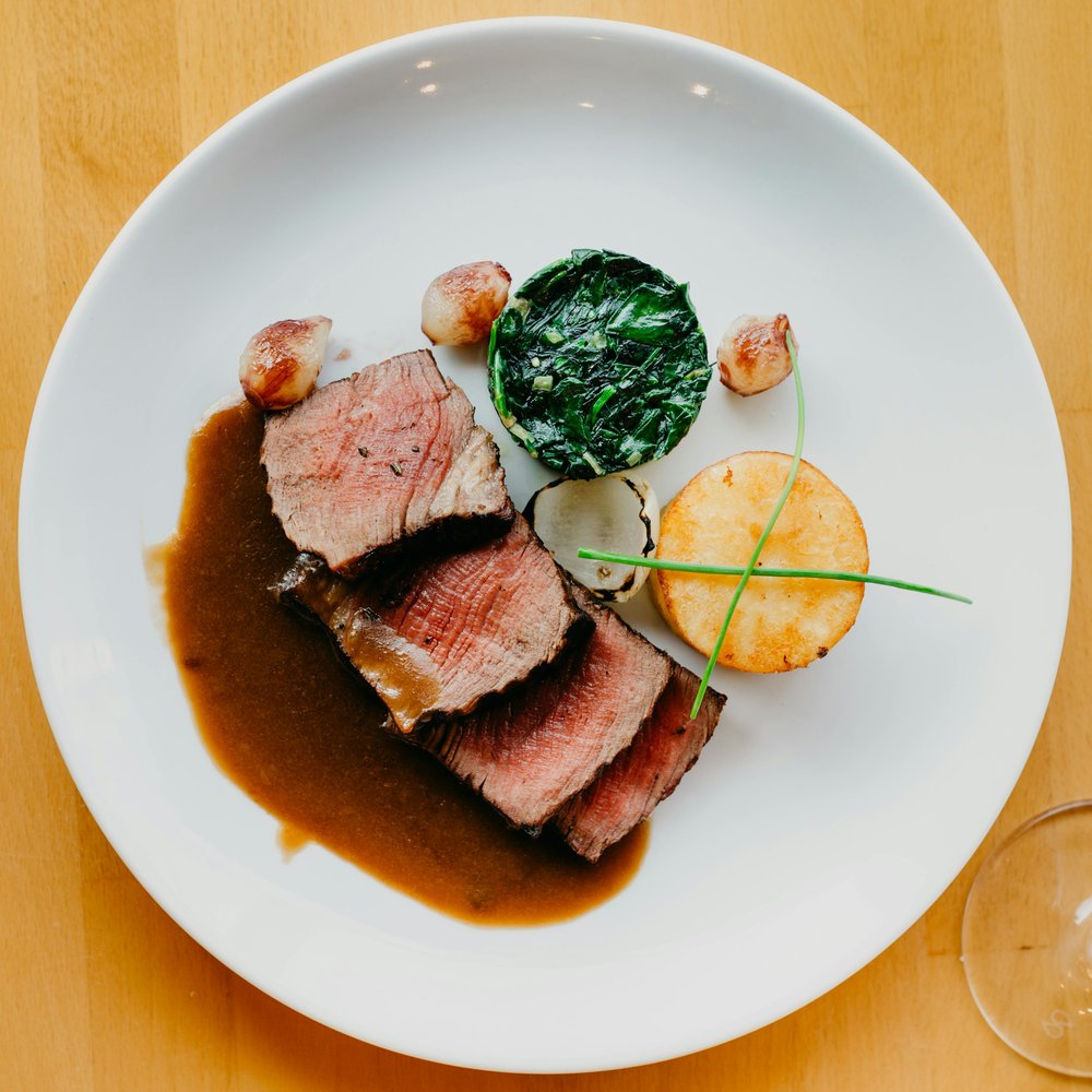 Sliced eye fillet steak with greens and sauce on white plate