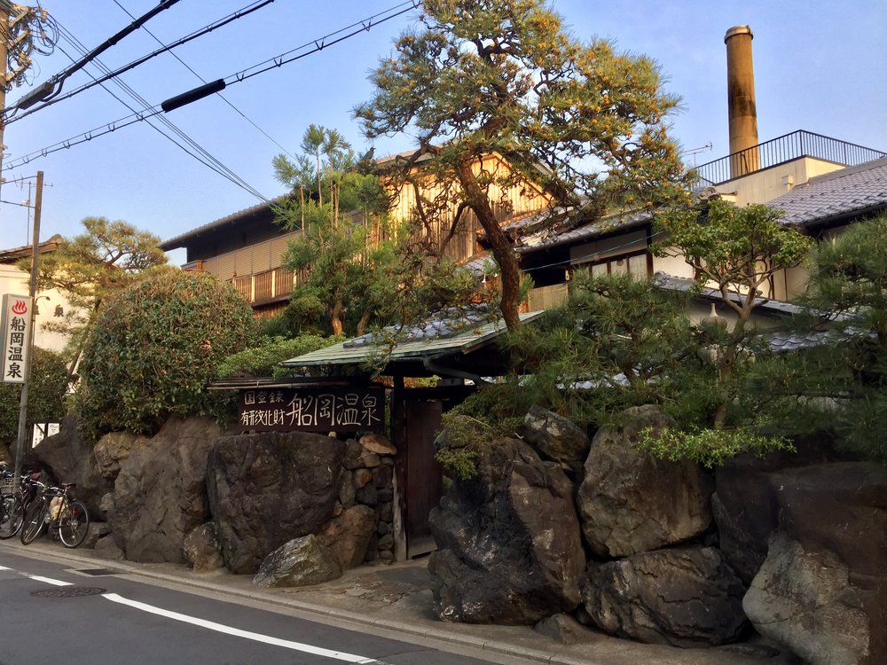 The entrance of Funaoka Onsen, a traditional Japanese hot spring bathhouse, surrounded by lush greenery and rocks