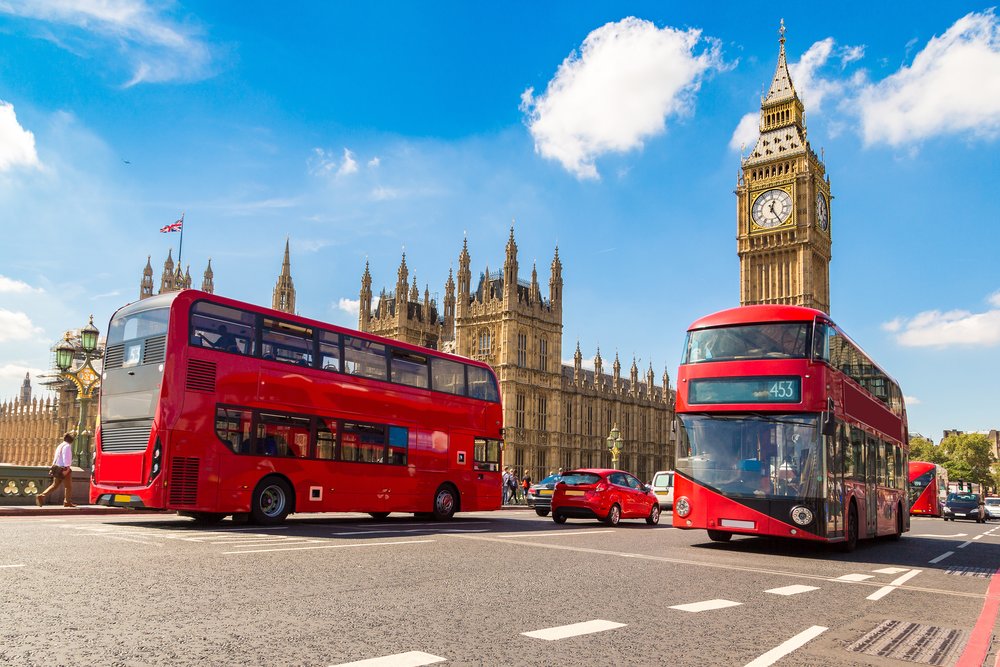 Red double-decker bus passing by Big Ben in London, with clear skies
