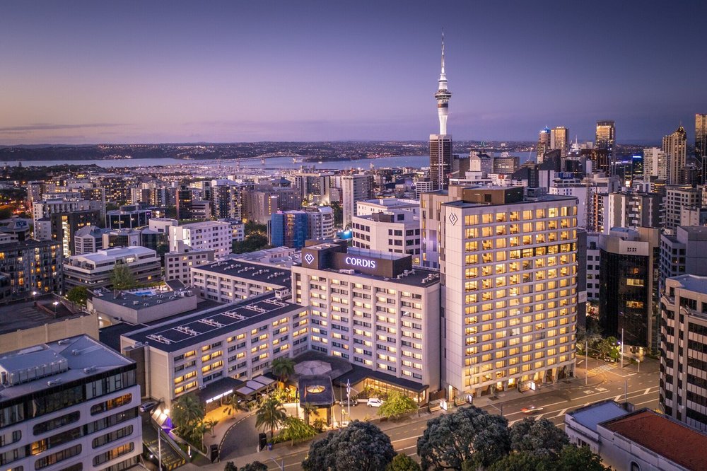 Cordis Auckland hotel building with Auckland skyline and Sky Tower at dusk
