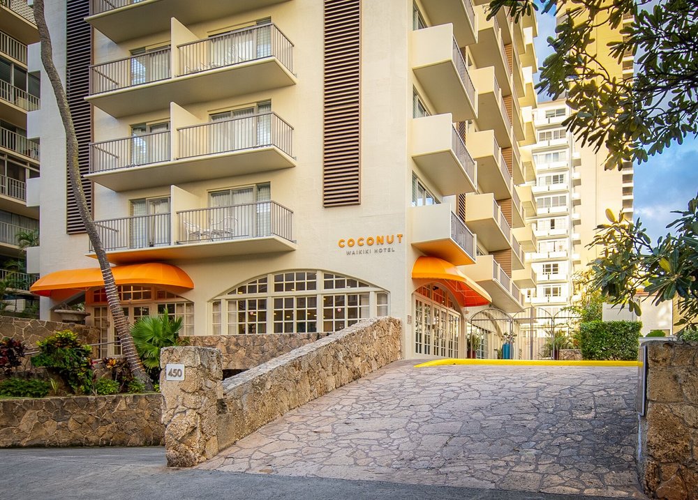 A driveway leading to a multi-level building with the words “Coconut Waikiki Hotel” on the front.