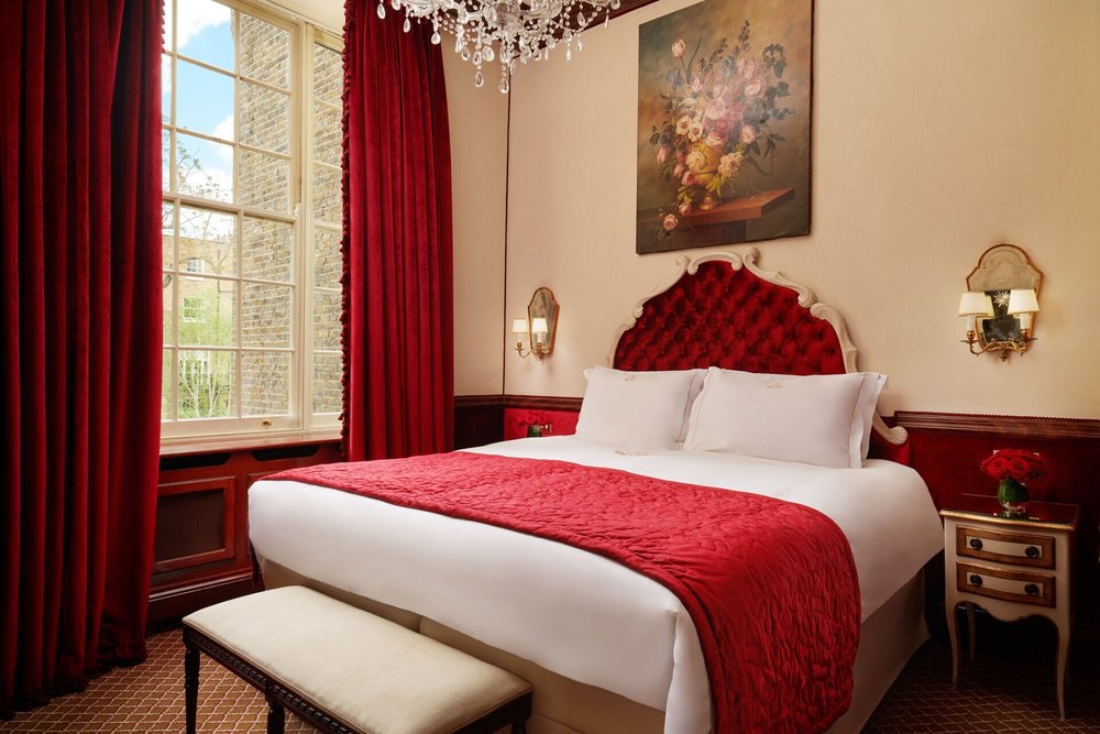A red-themed hotel room with a vintage touch, featuring a plush bed and chandelier.