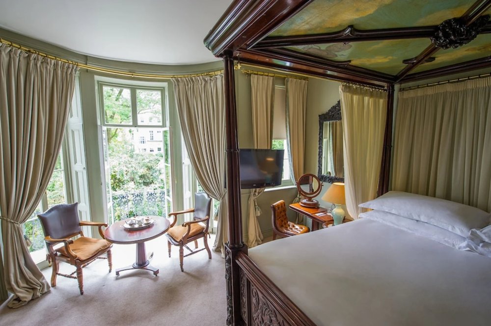 Luxurious hotel room with a four-poster bed, Victorian-style furnishings, and a beautiful view