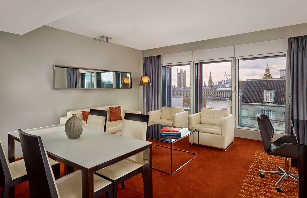 Hotel suite with a modern living area, large windows, and views of the Big Ben and Thames River