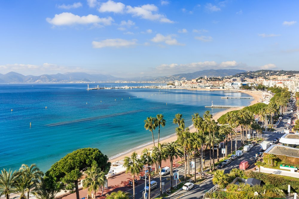 Cannes beachfront with clear water, palm trees, and the iconic coastline