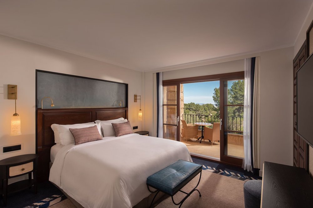 Spacious room with elegant decor and a balcony overlooking lush greenery at Hotel Son Vida, Mallorca